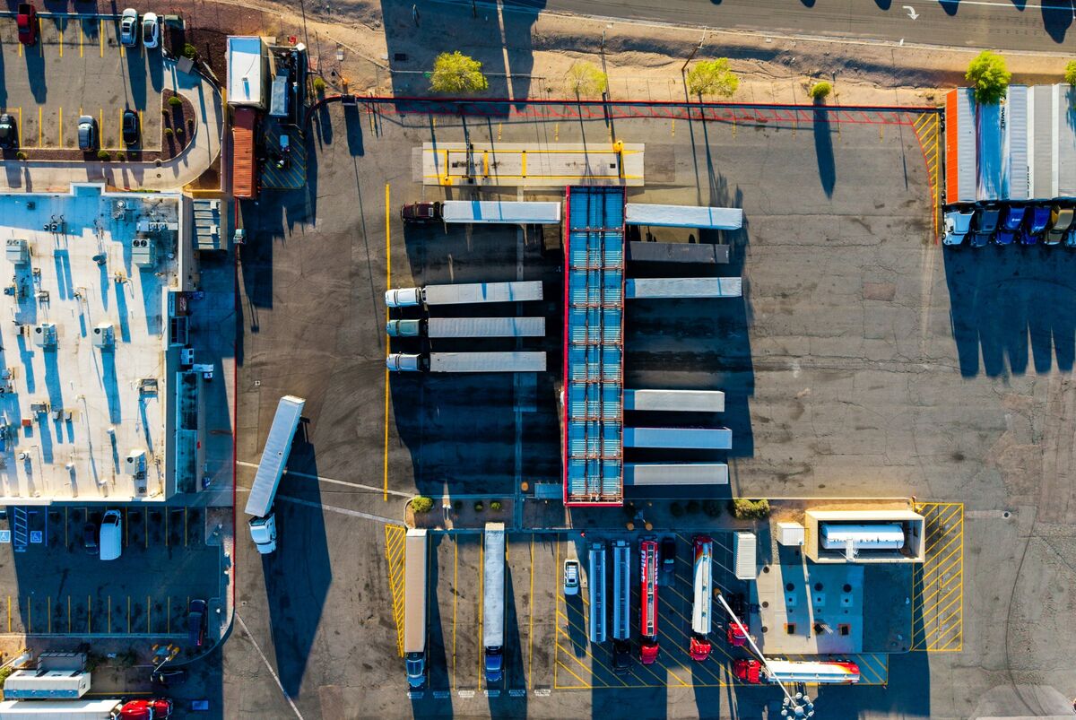 Caminhão de cargas sendo abastecido ao lado de documentos de custos de transporte em um terminal logístico.