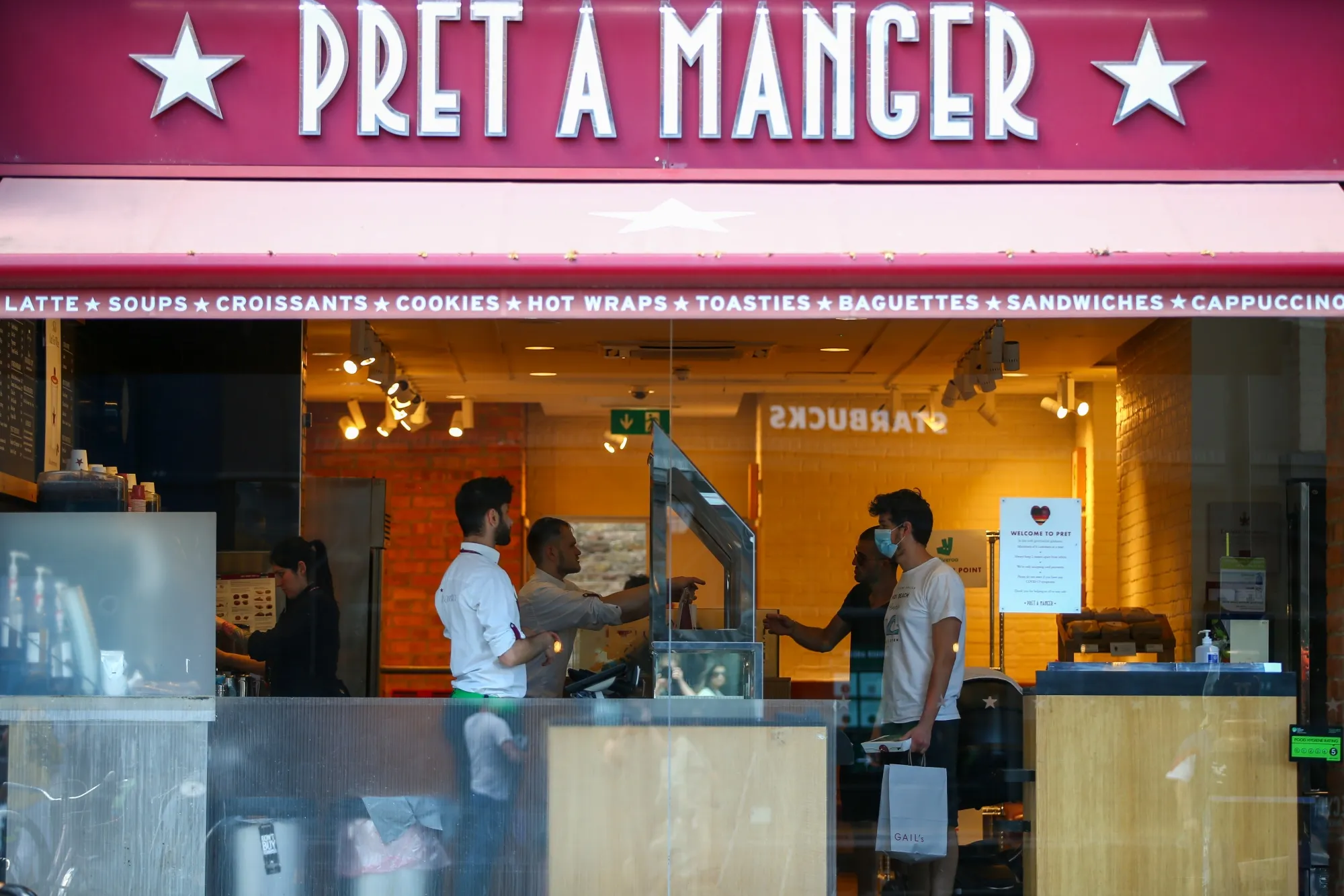 Employees stand behind a protective screen as they serve customers at a reopened Pret A Manger Ltd. store in London.