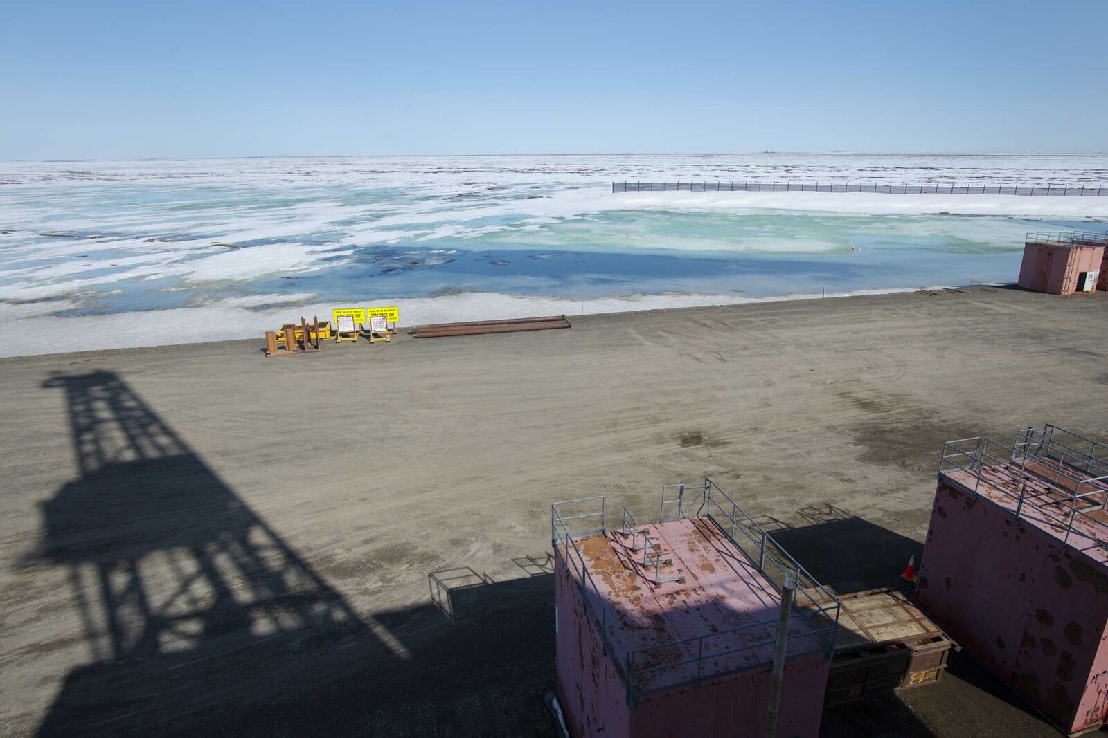 The shadow of Doyon Drill Rig 142 is cast on the gravel pad beside several oil wells at the Kuparuk oil field on Alaska’s North Slope.
