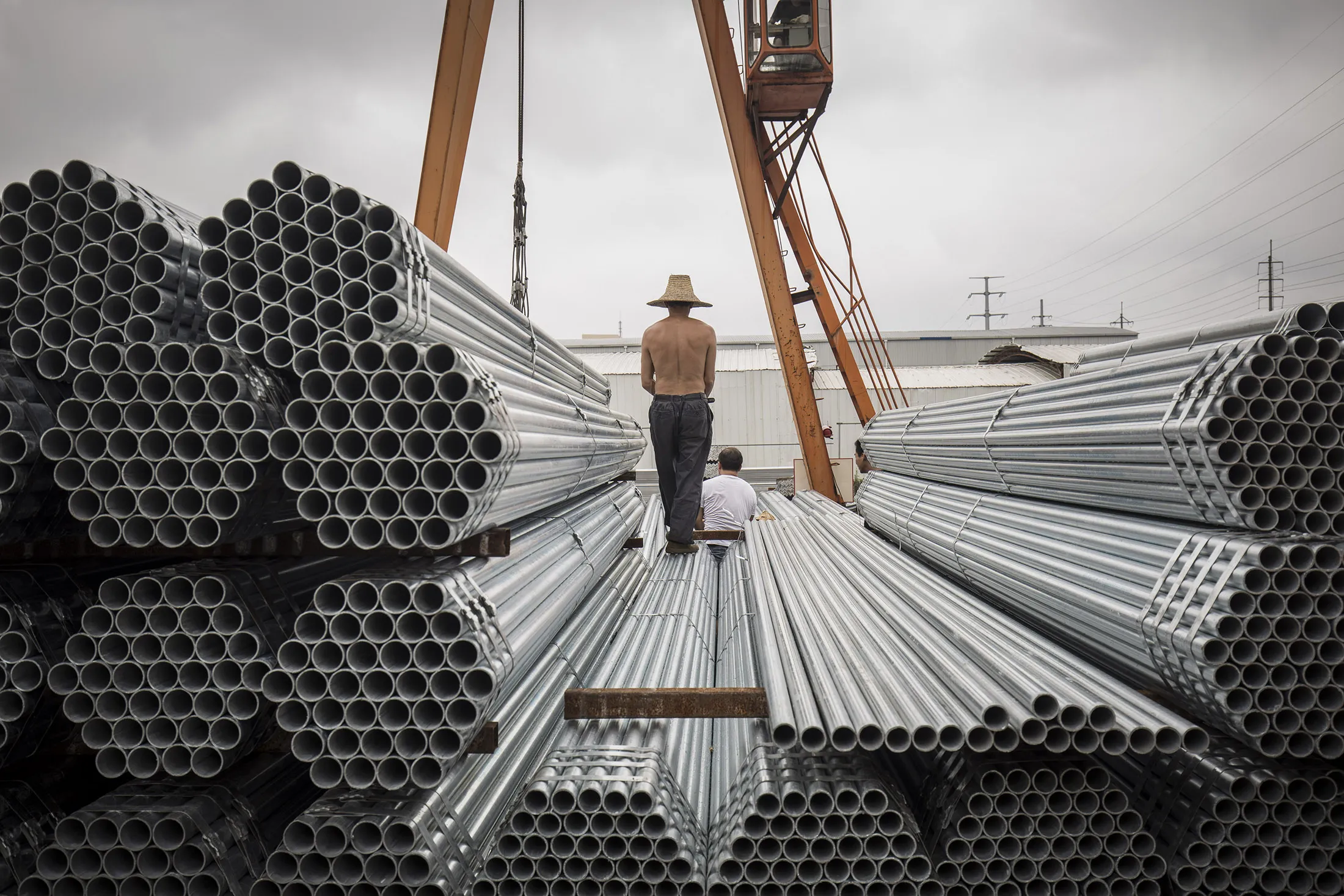 Workers prepare to lift bundles of steel pipe with a crane at a stockyard on the outskirts of Shanghai, China.