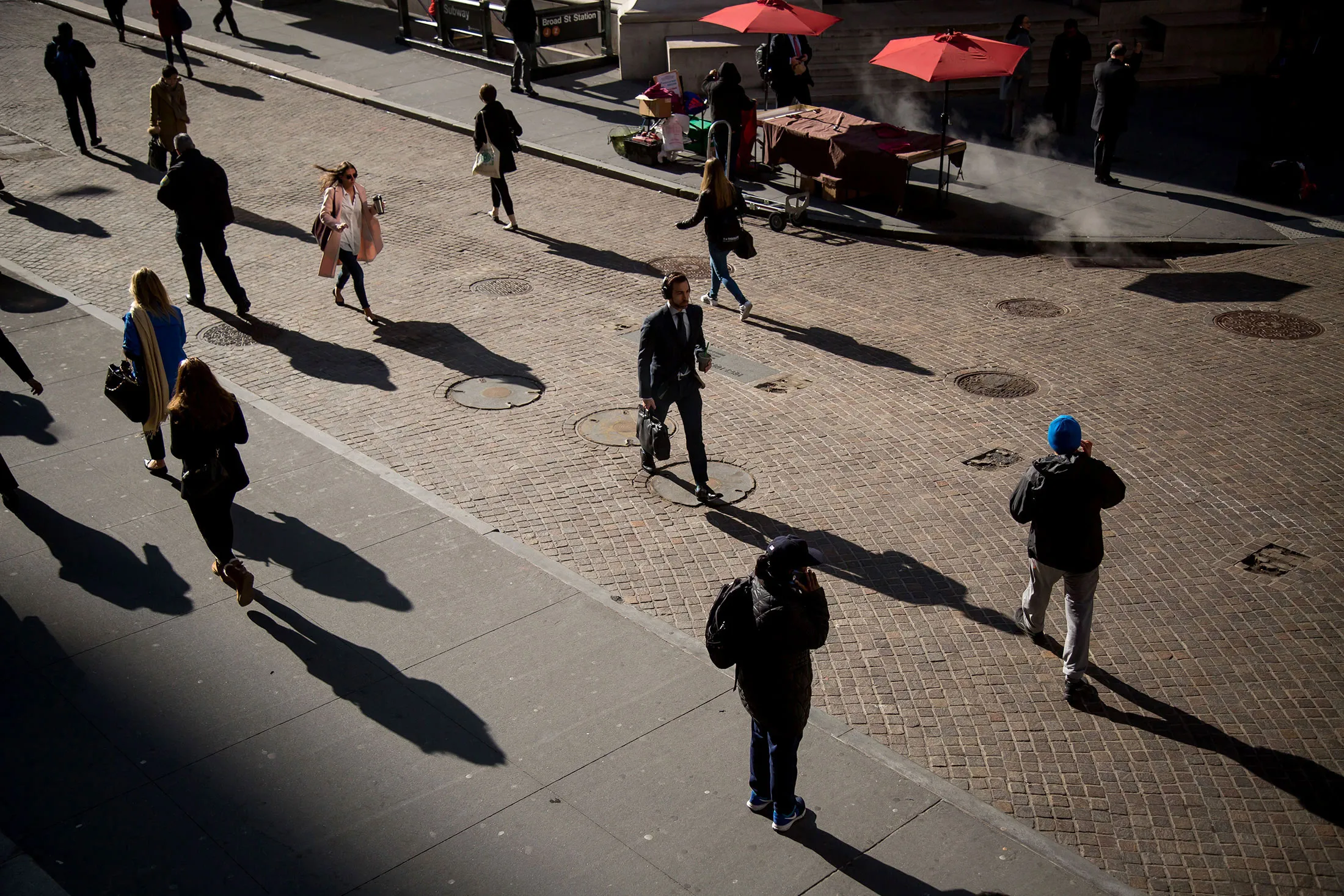 Pedestrians cast shadows as they walk on Wall Street near the New York Stock Exchange (NYSE) in New York, U.S., on Monday, March 7, 2016. U.S. stocks fluctuated near two-month highs as commodity shares surged with crude oil, offsetting declines among technology and consumer companies as investors assessed China's growth prospects.
