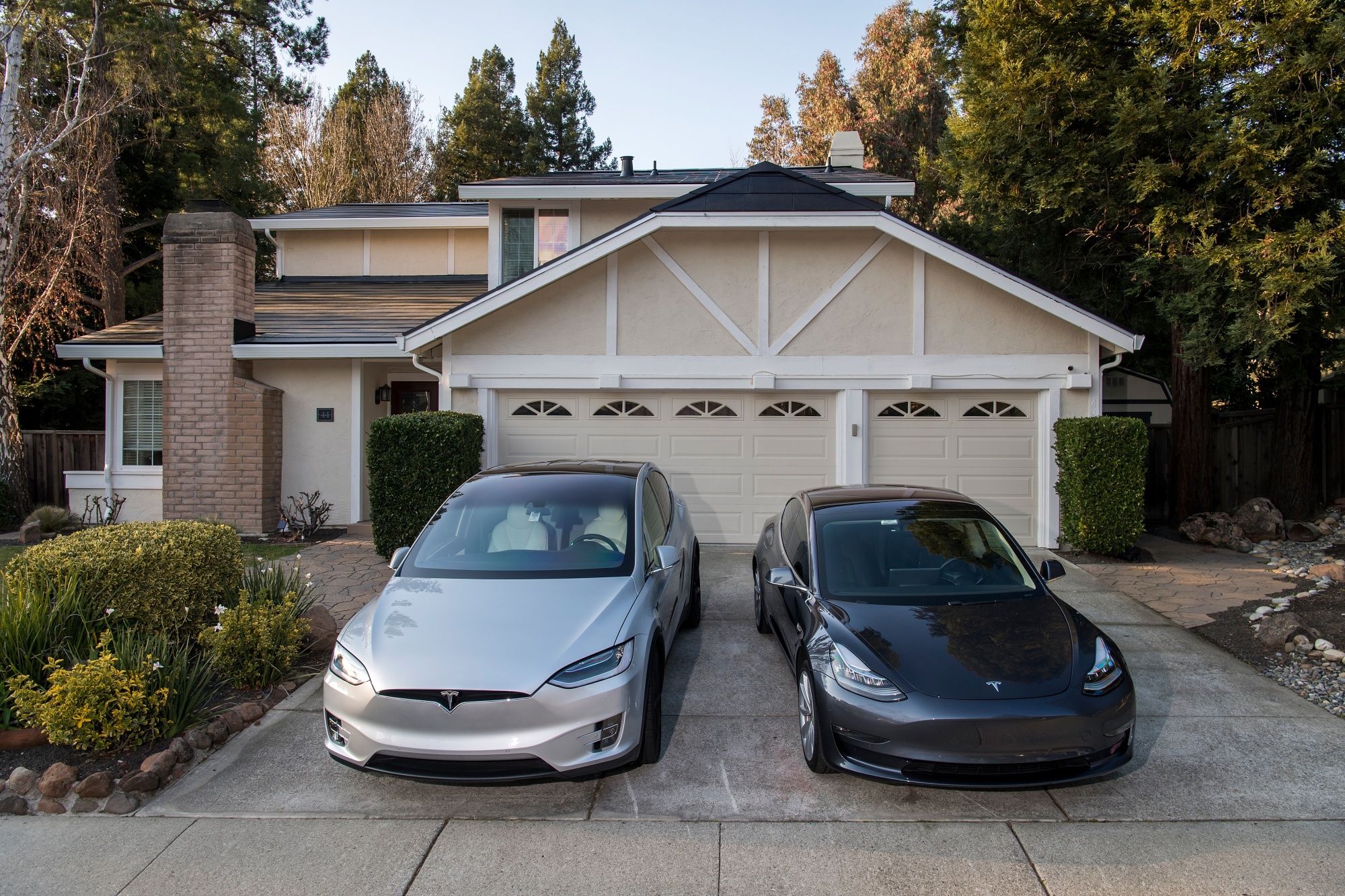 Tesla Model X and Model 3 cars in the driveway of a home with a Tesla Solar Roof in California.