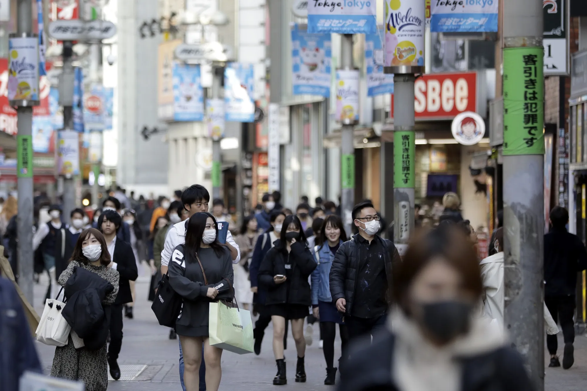 Pedestrians wearing protective masks walk past shops in the Shibuya district of Tokyo&nbsp;on March 26.