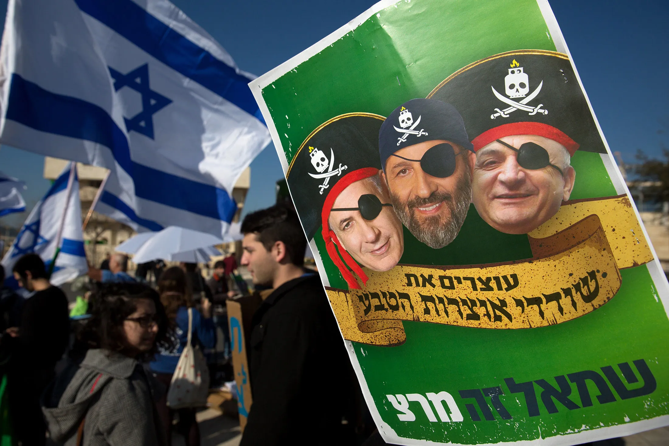 A protester holds a placard bearing portraits of (from left) Israeli Prime Minister Benjamin Netanyahu, Interior Minister Aryeh Deri, and businessman Isaac&nbsp;Tshuva on Feb. 3, 2016, in front of the Supreme Court in Jerusalem where a hearing took place on a contentious natural gas deal.
