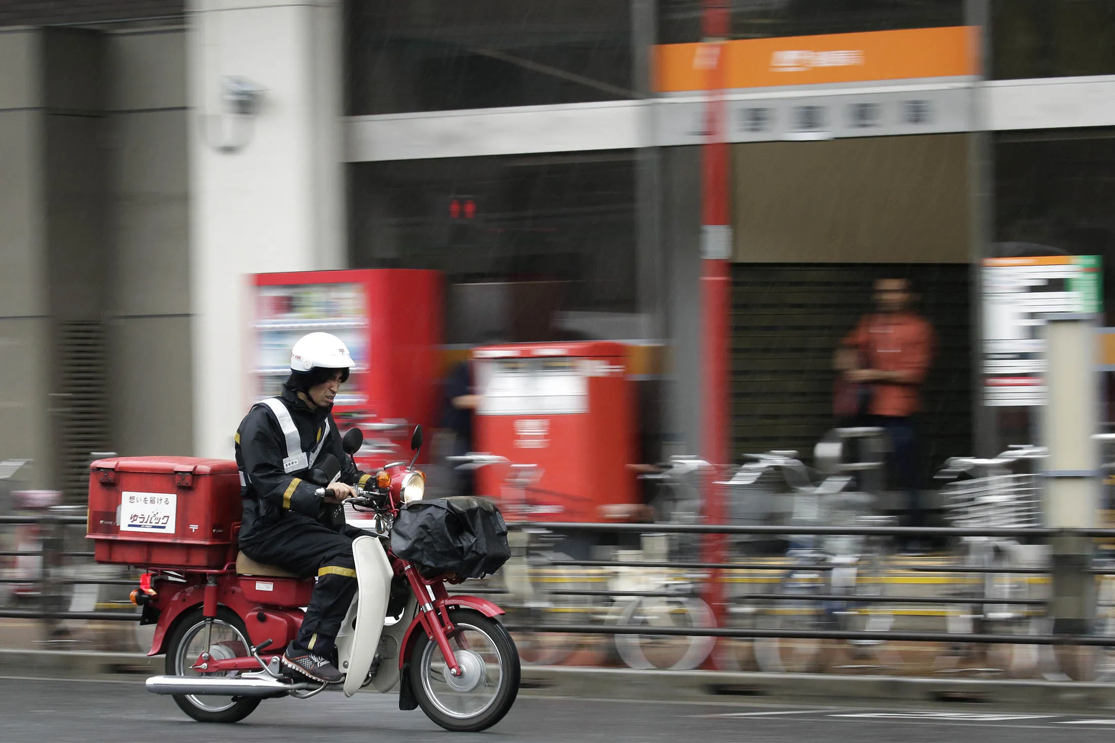 A Japan Post mail carrier rides a motorcycle.
