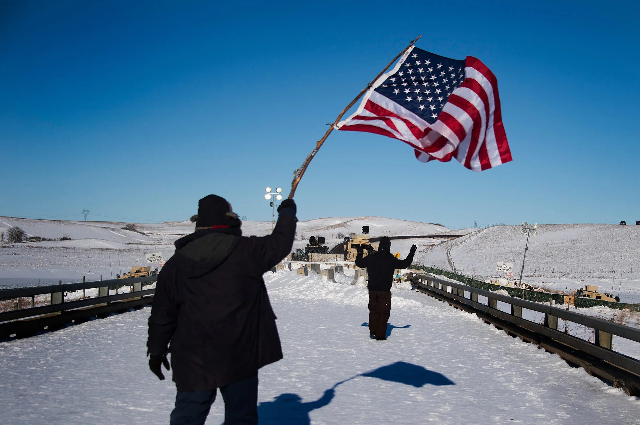 A protester waves an American flag as an activist approaches the police barricade with his hands up on a bridge near Oceti Sakowin Camp on the edge of the Standing Rock Sioux Reservation.
