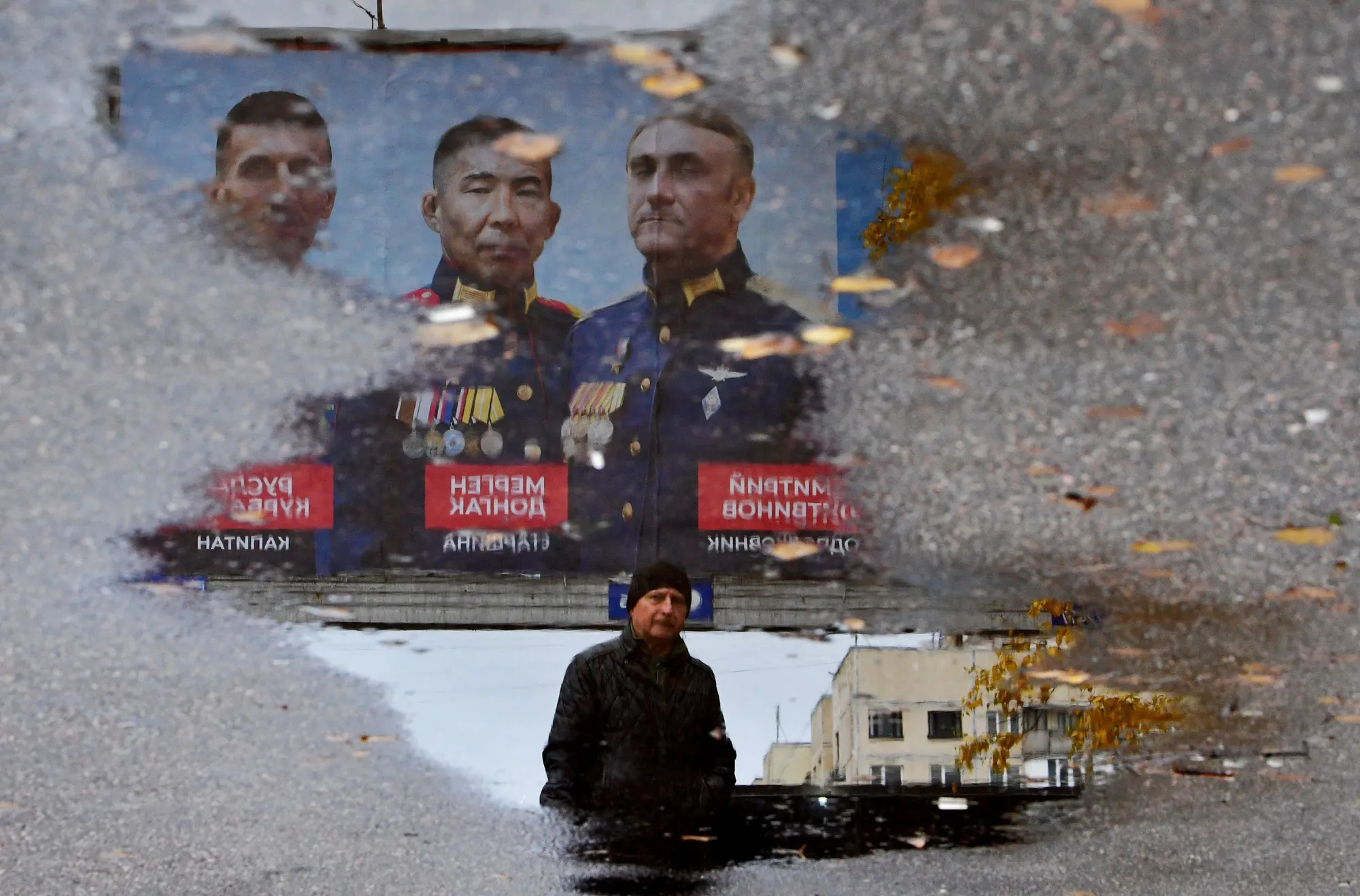 A man walks past a billboard depicting&nbsp;portraits of Russian Army officers,&nbsp;reflected&nbsp;in a puddle,&nbsp;in Saint Petersburg, Russia, on Nov. 8.