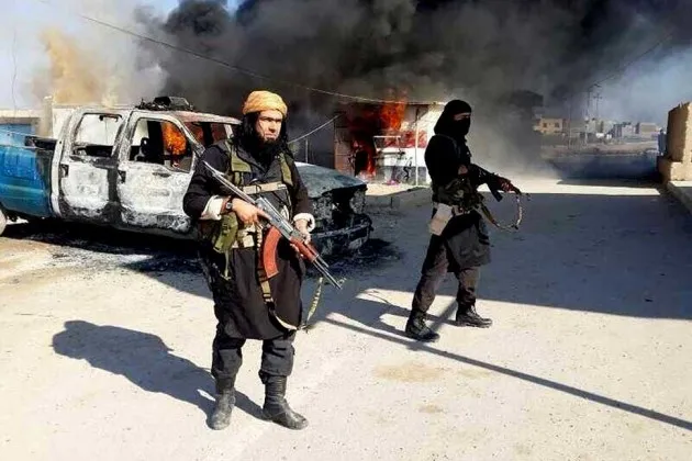 Members of the Islamic State of Iraq and the Levant (ISIL) next to a burning police vehicle in Iraq's Anbar Province