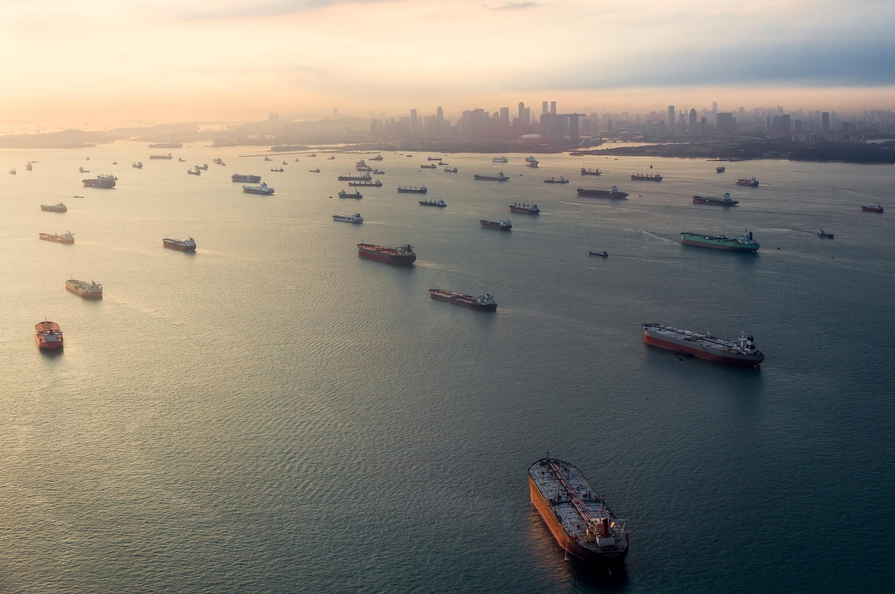 Empty cargo ships sit idle in the Singapore Strait as the sun sets over a hazy Singapore skyline. Photographer: Peter Novacco/Getty Images