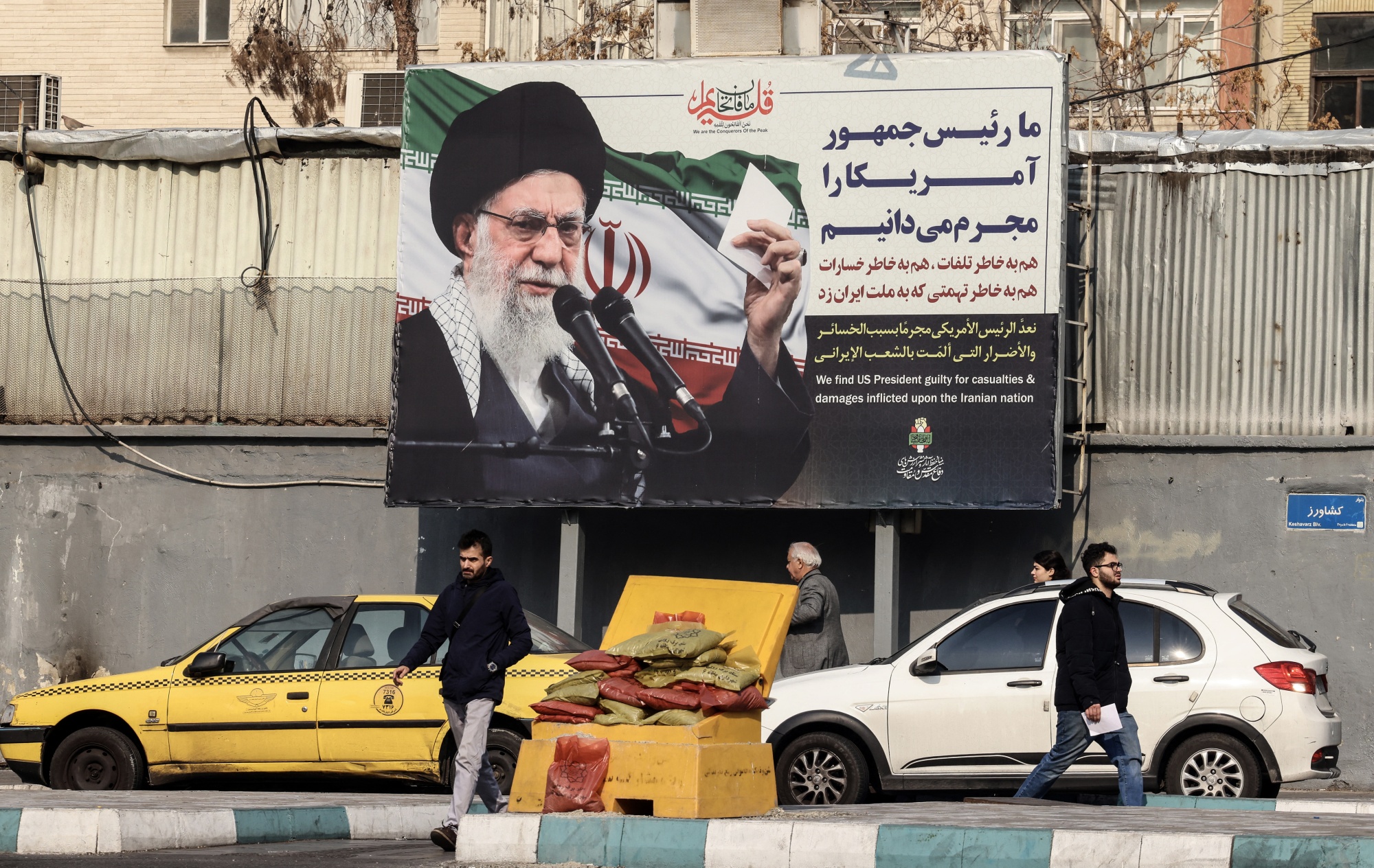 Iranians walk past a billboard showing Iranian supreme leader Ayatollah Ali Khamenei with anti-US rhetoric in Tehran on January 27, 2026. A US naval strike group led by an aircraft carrier has deployed to Middle Eastern waters, the United States said on January 26, 2026, as Tehran warned it was ready to hit back at any American attack launched in response to a crackdown on anti-government protests. (Photo by ATTA KENARE / AFP via Getty Images) Photographer: ATTA KENARE/AFP