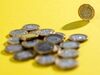 A one pound coin stands next to a pile of coins in this arranged photograph.