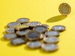 A one pound coin stands next to a pile of coins in this arranged photograph.