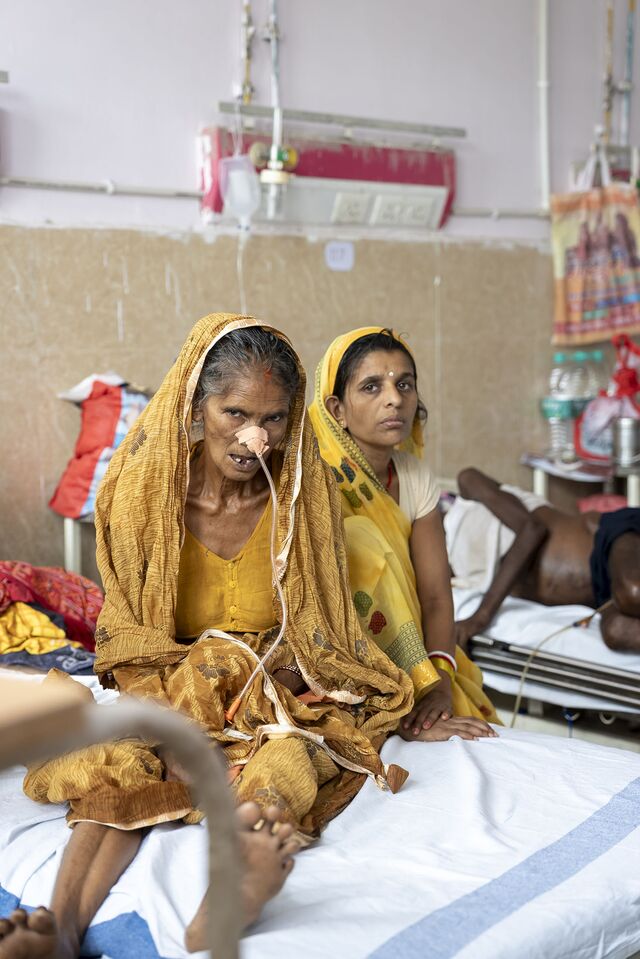 A patient and her family member sit on a bed in the general ward at ANMMCH
