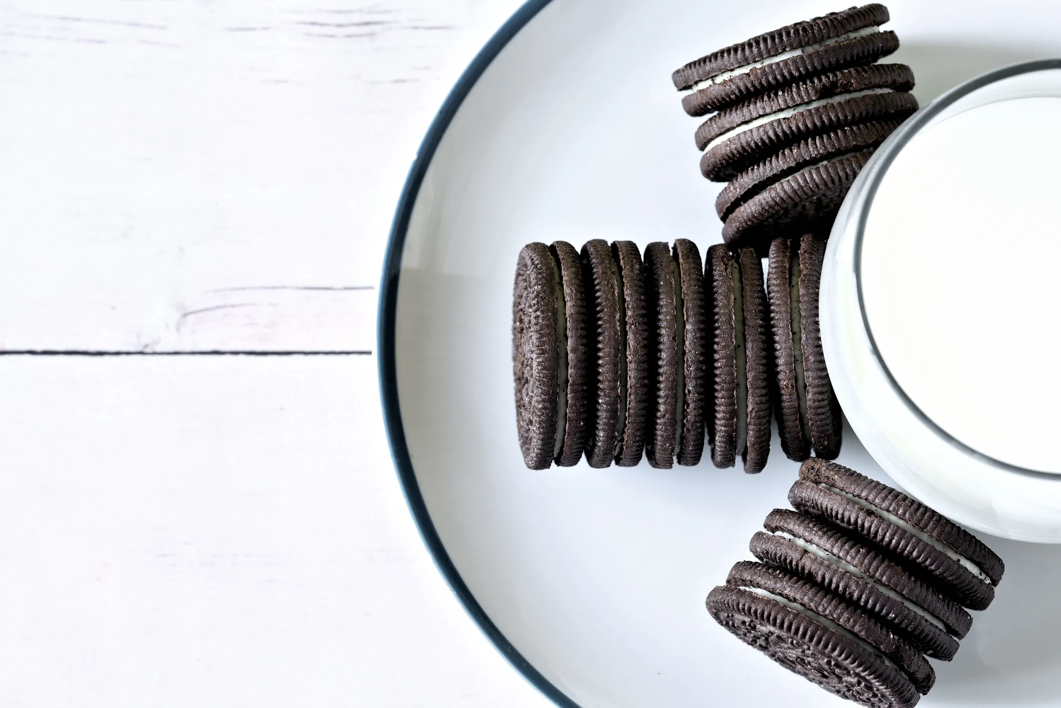 Chocolate sandwich cookies arranged on a plate with a glass of milk