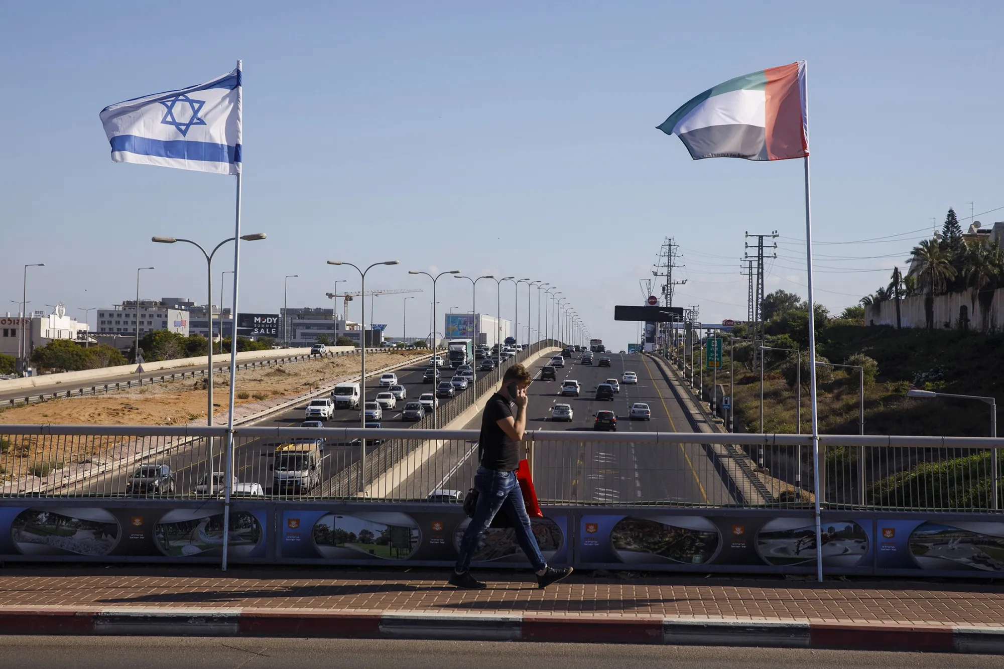 A pedestrian walks by Israeli and UAE&nbsp;flags&nbsp;on the side of a road in Netanya, Israel, on Aug. 17.