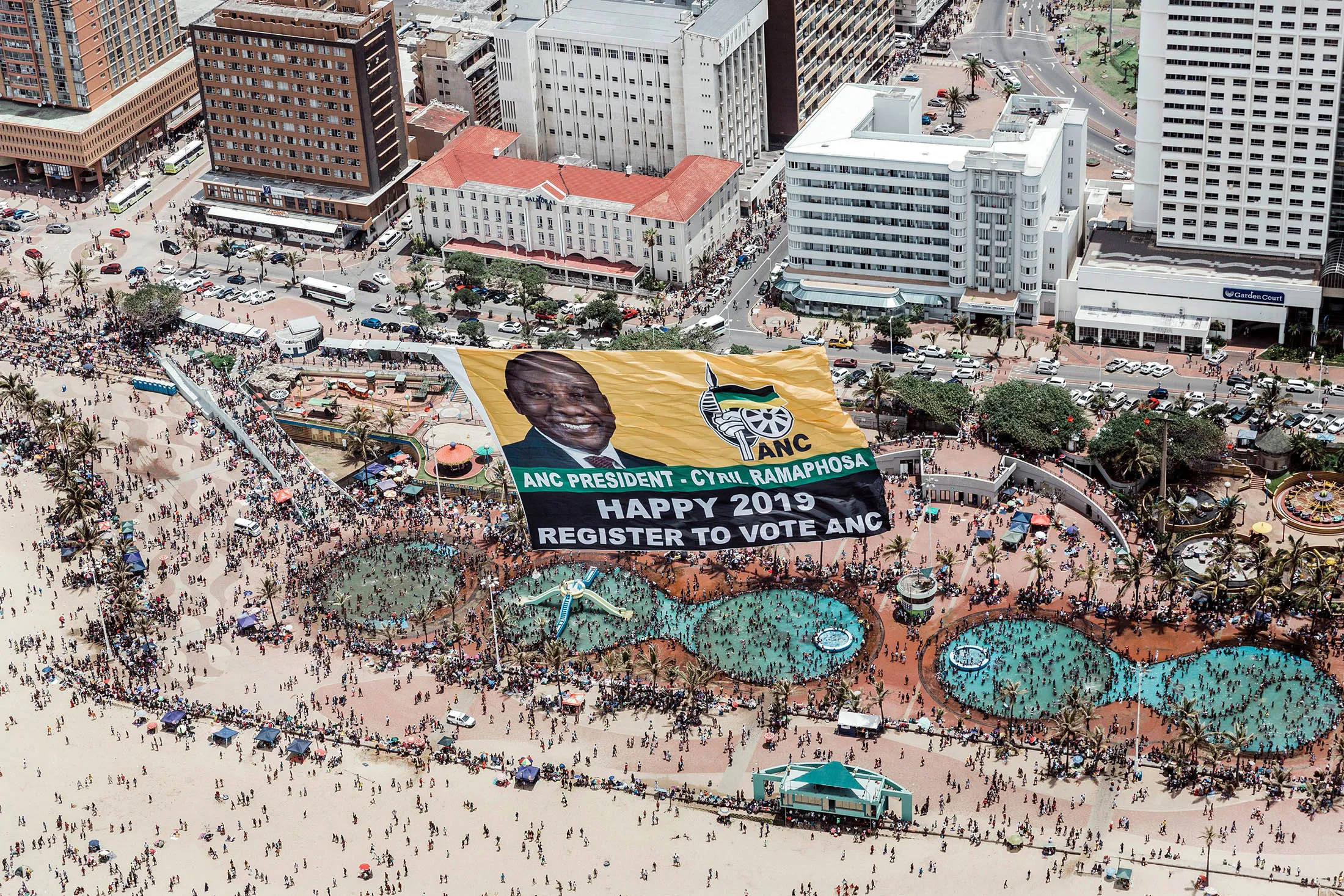 A helicopter pulls a flag displaying the image of Ramaphosa and urging people to register. 