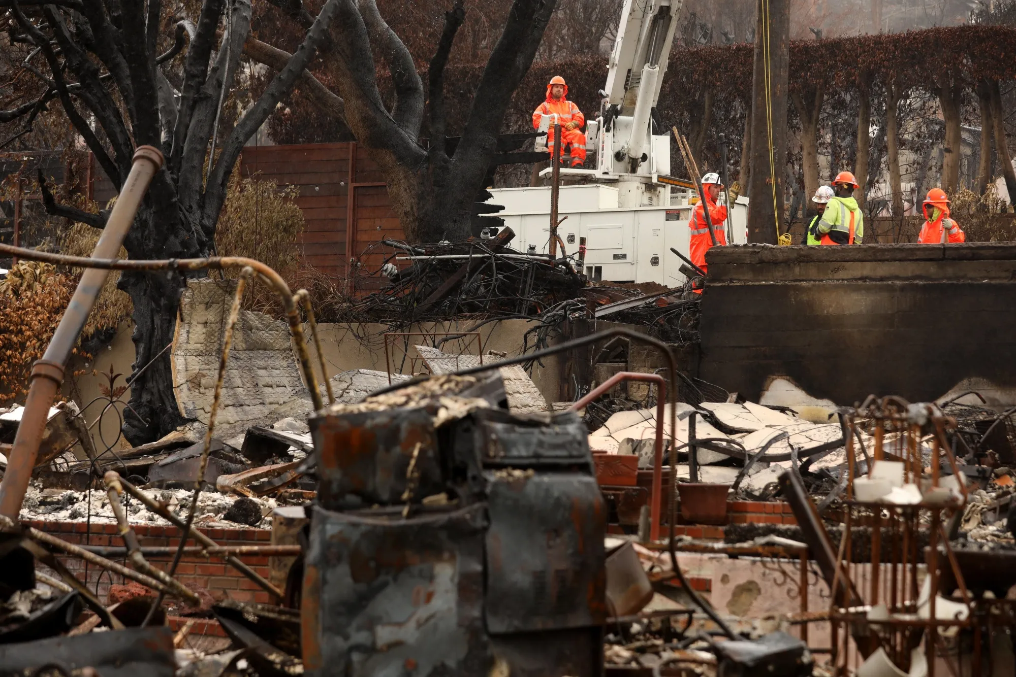 Workers with the Los Angeles Department of Water and Power work among debris of fire-ravaged homes in Pacific Palisades in 2025.