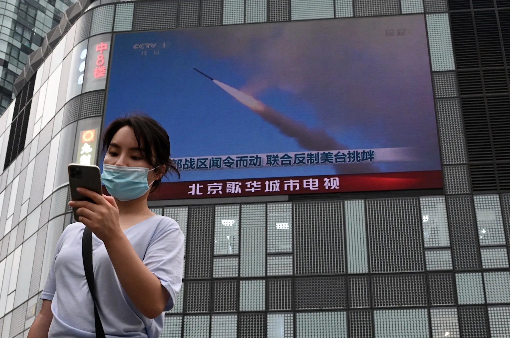A woman walks by a screen showing China's military exercises around Taiwan.&nbsp;