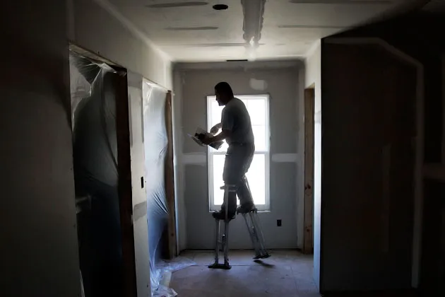 Raul Rios, wearing a pair of stilts, applies joint compound to the seams of drywall at a house under construction in Raleigh, N.C.
