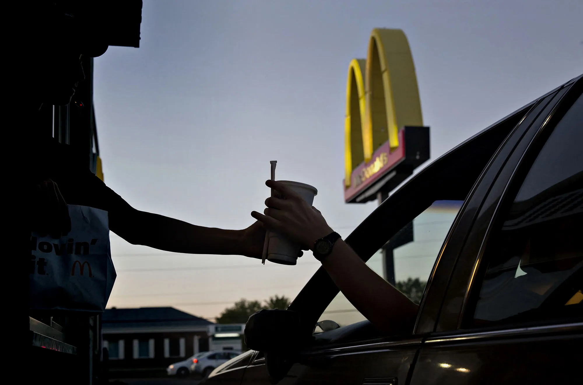 An employee hands a beverage to a customer at the drive-thru window of a McDonald's Corp. restaurant in Peru, Illinois.