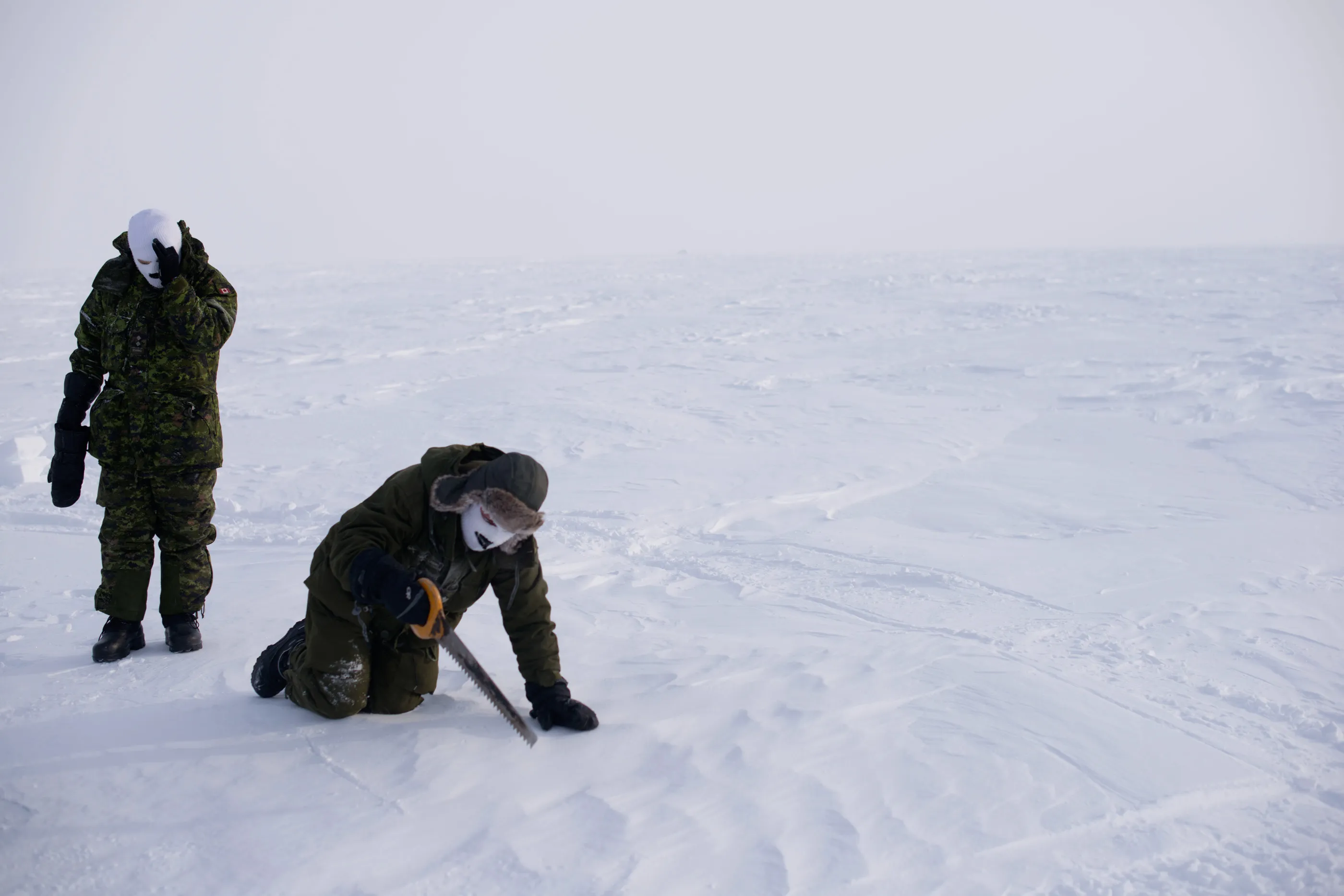 Canadian soldiers saw into the icy snow-covered landscape to test ice for building blocks near Sanirajak in Nunavut.  Survival techniques chew up time.