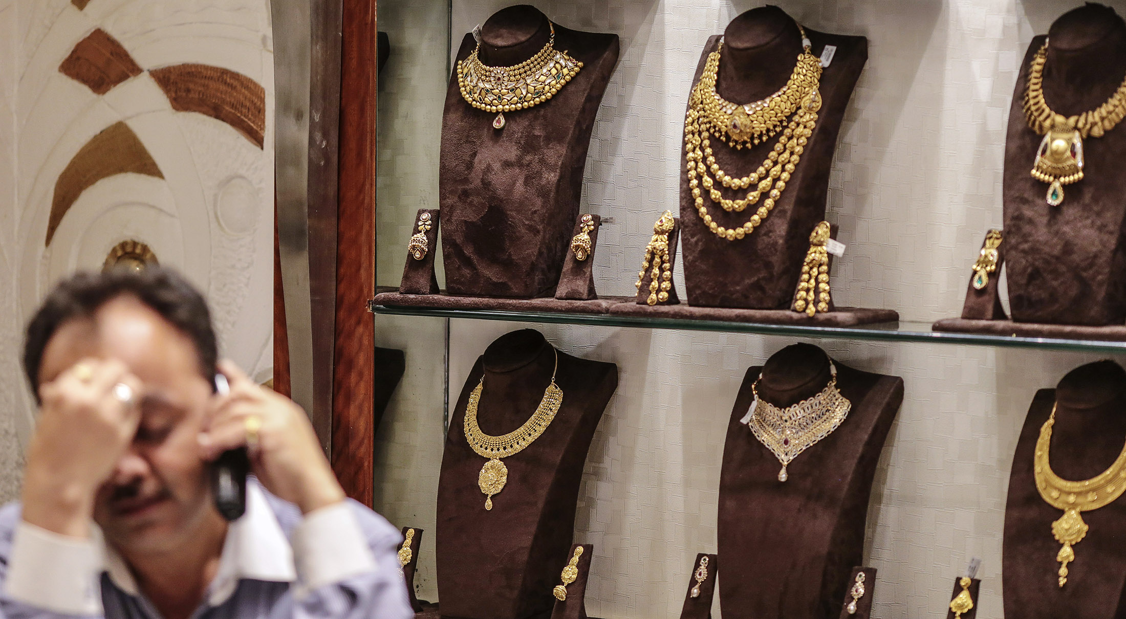 Gold necklaces sit on display as an employee talks on the phone inside the Dwarkadas Chandumal Jewelers store in the Zaveri Bazaar area of Mumbai, India, on April 21, 2015.
