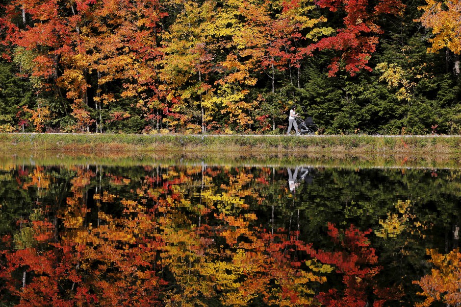 A woman pushes a baby stroller around Dream Lake amid fall foliage in Amherst, New Hampshire.