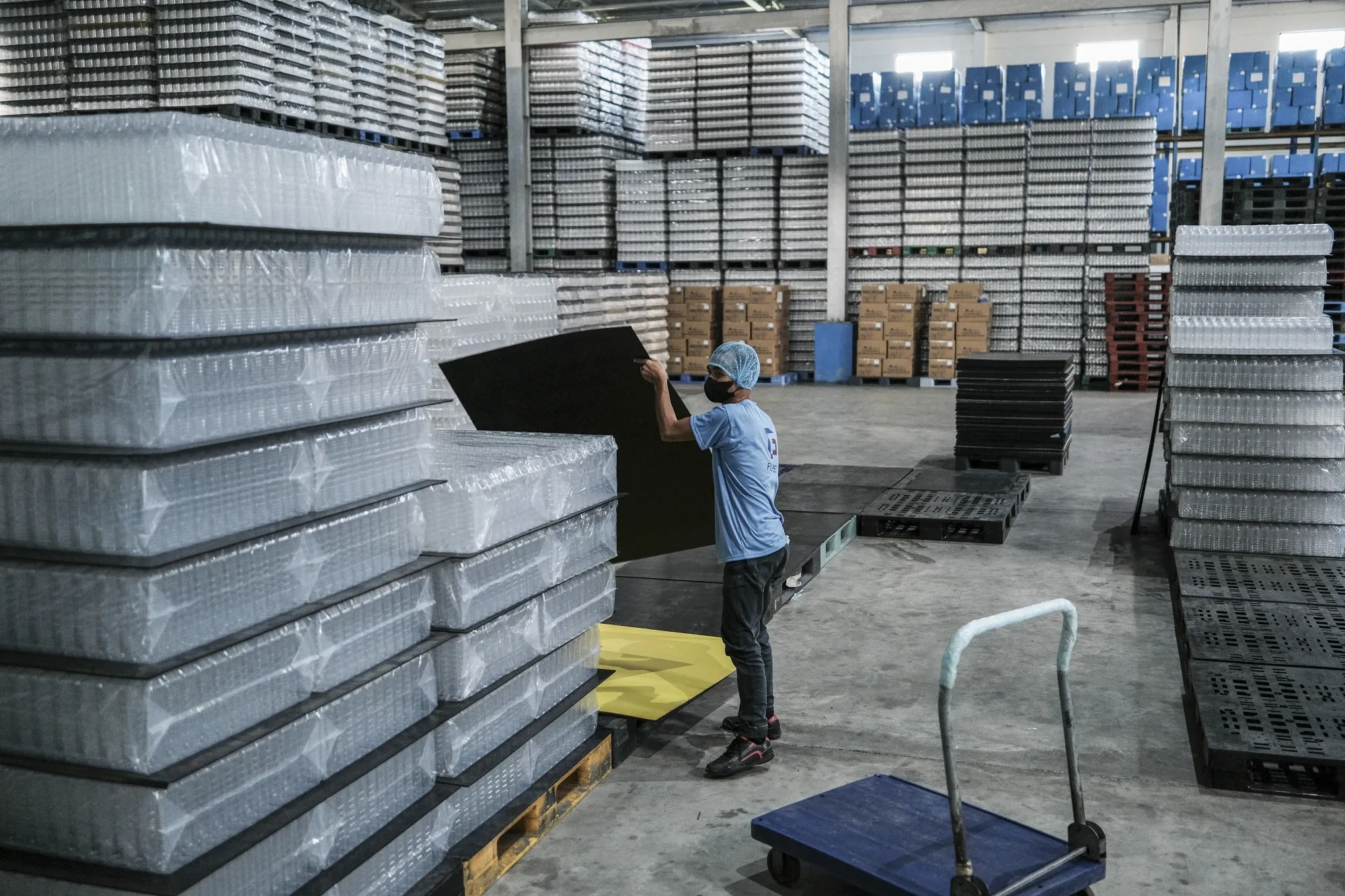 An employee handles stacks of Polyethylene terephthalate bottles at a plastics production facility in the Philippines.