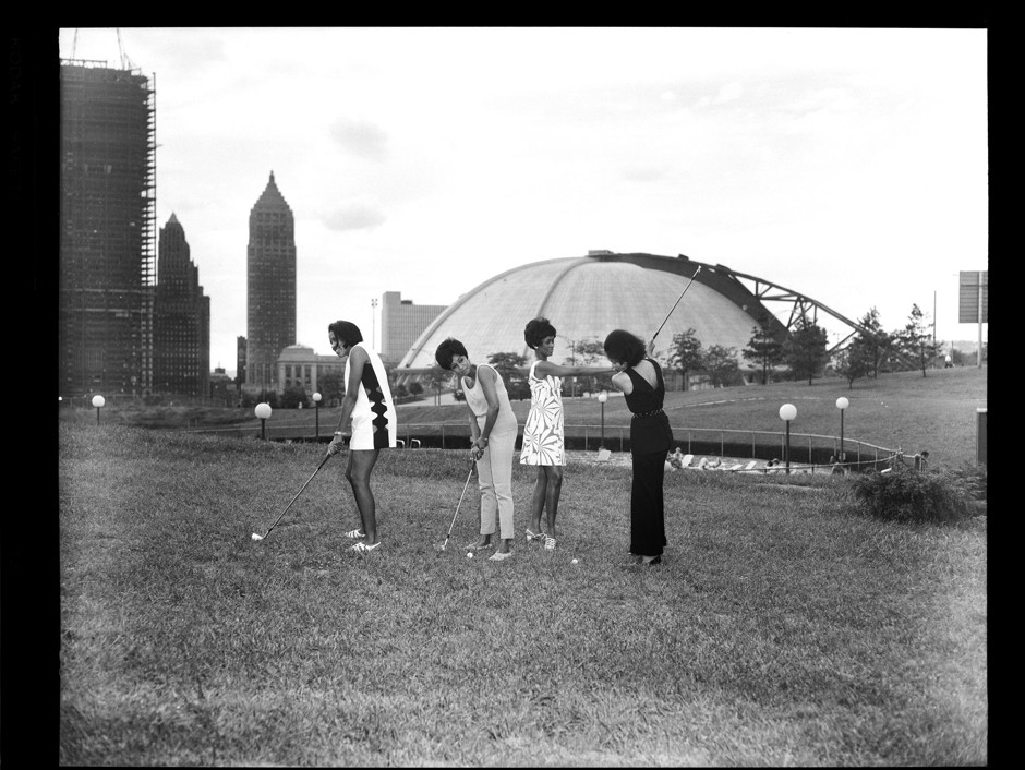 Lynette May, Gerri Walker, Shirley Jenkins, and Alberta Thompson hitting golf balls at the Washington Plaza putting field, with Civic Arena in the background, 1969.