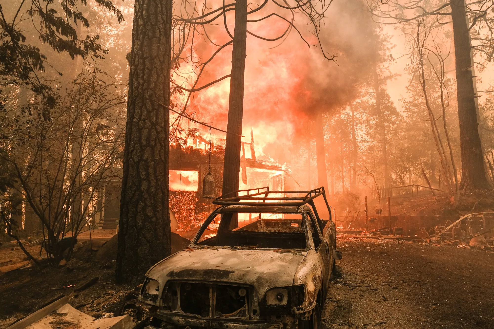 A structure burns behind a charred vehicle on Jerseydale road during the Oak Fire in Mariposa County, California,&nbsp;on July 23, 2022.&nbsp;