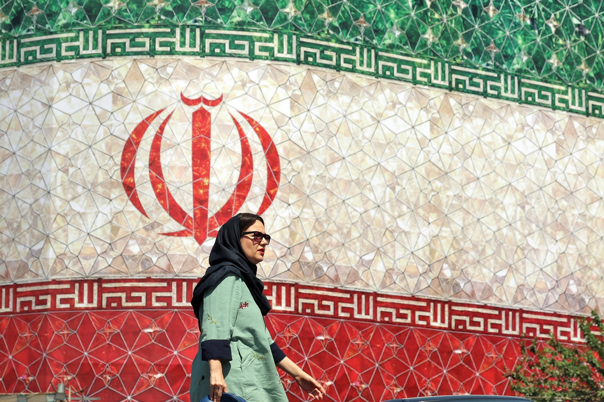 An woman walks past a billboard displaying Iran's national flag at Enghelab Square in Tehran