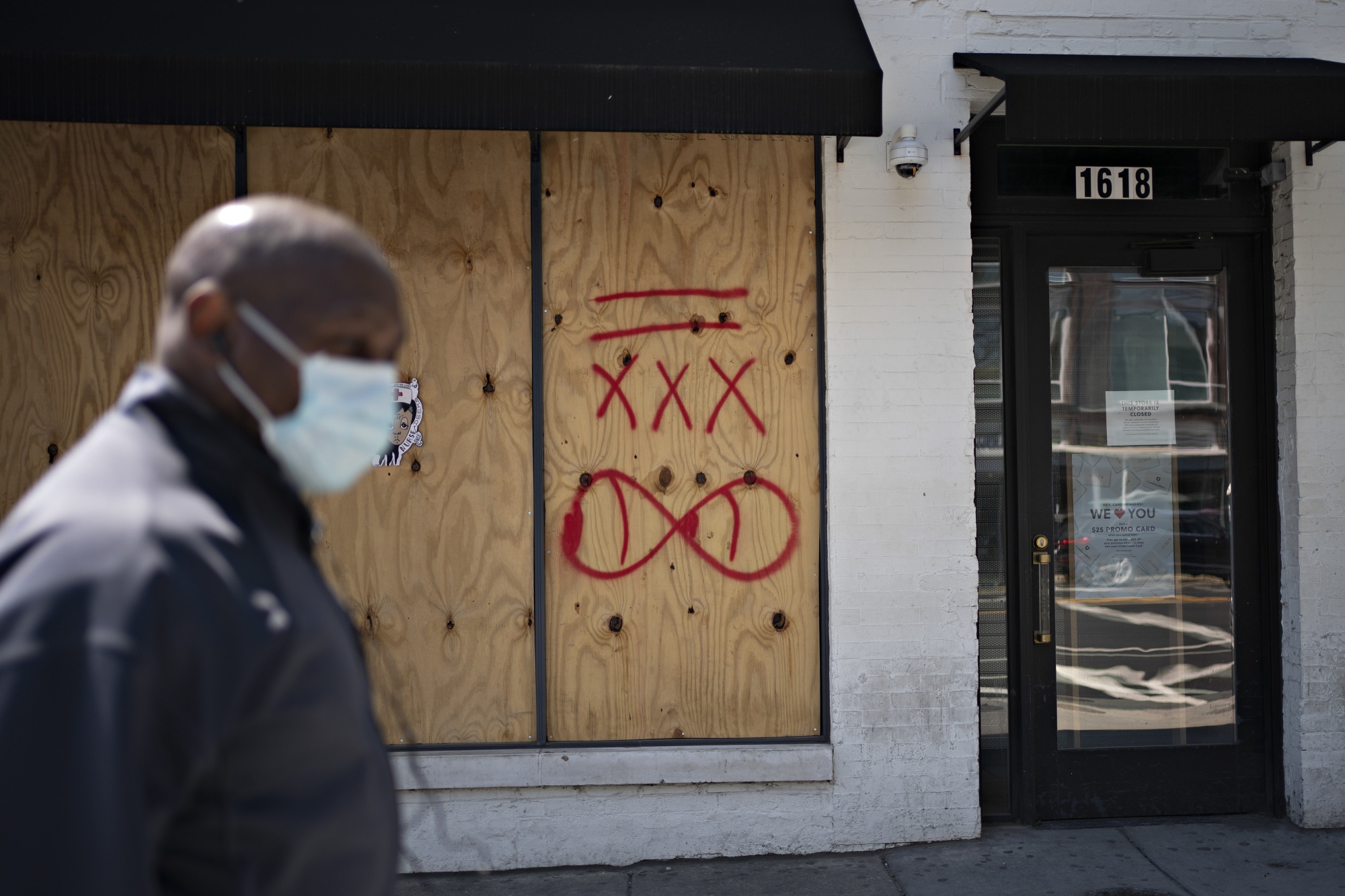 A pedestrian wearing a protective mask walks past a boarded up J. Crew Group Inc. store in Washington, D.C.