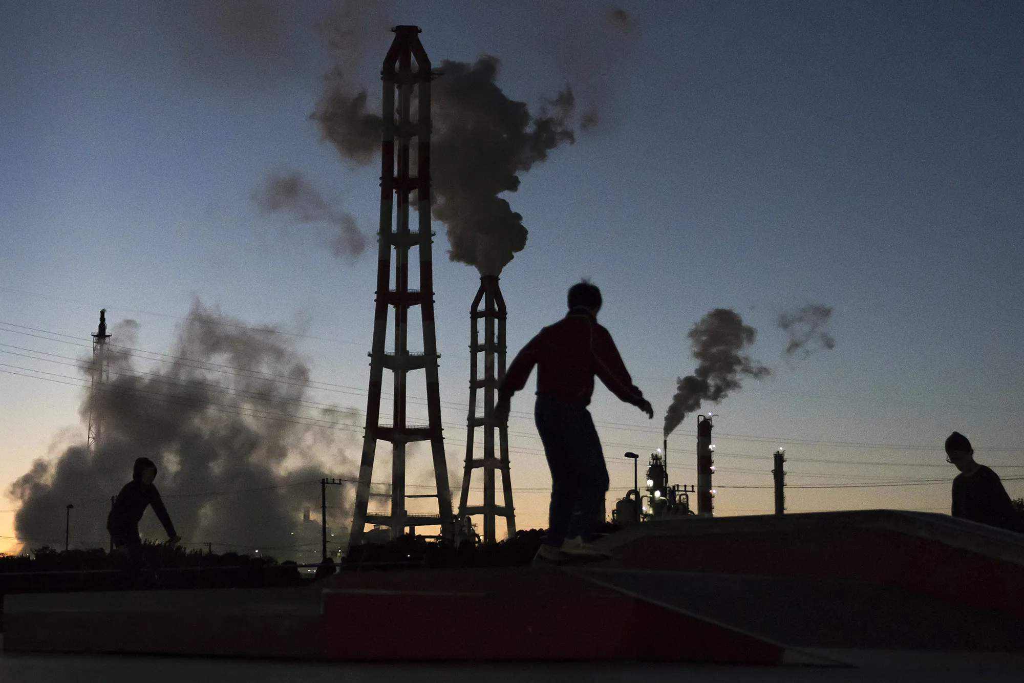 Men walk in front of smoke rising from chimneys at factories at dusk&nbsp;in Kamisu, Ibaraki, Japan.&nbsp;