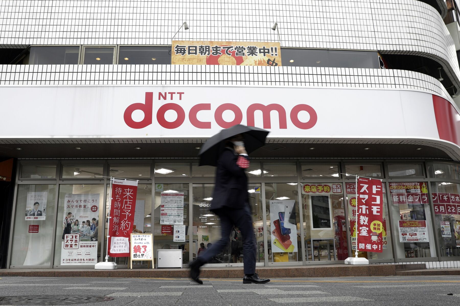 A pedestrian holding an umbrella walks past an NTT Docomo Inc. store in Tokyo, Japan.