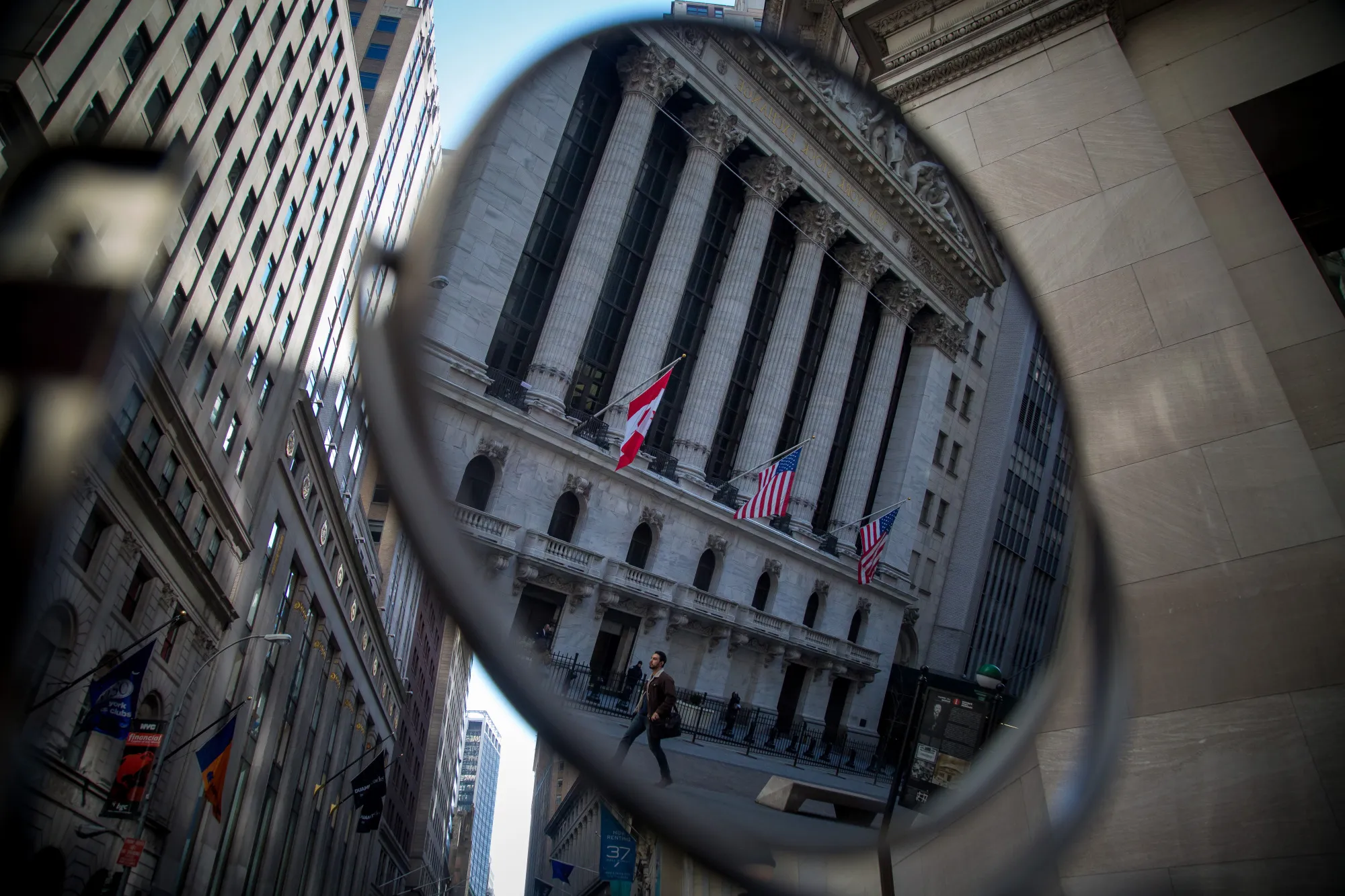 A pedestrian is reflected in a mirror while walking past the New York Stock Exchange.