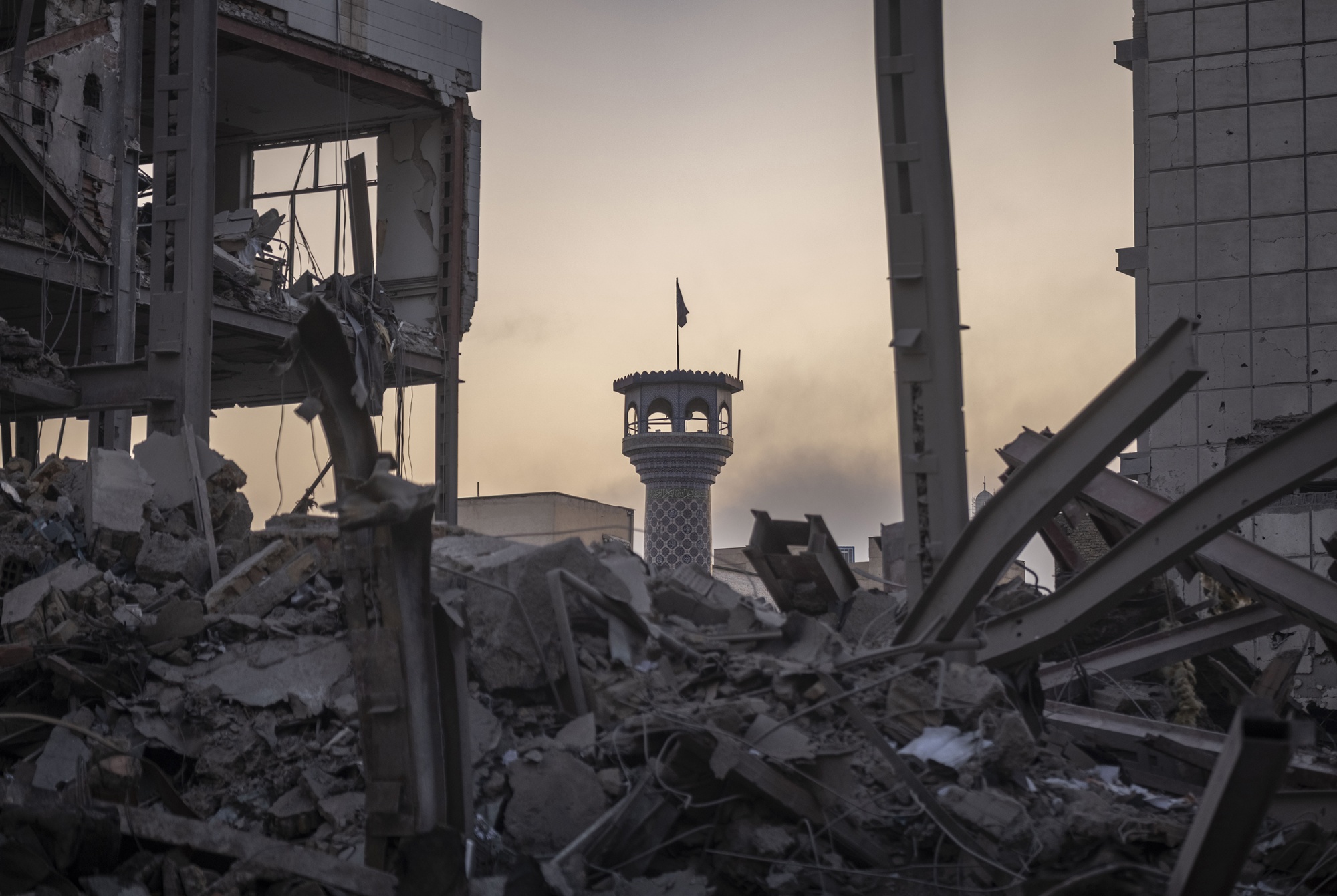 A minaret of a mosque rises behind a pile of twisted metal and rubble.