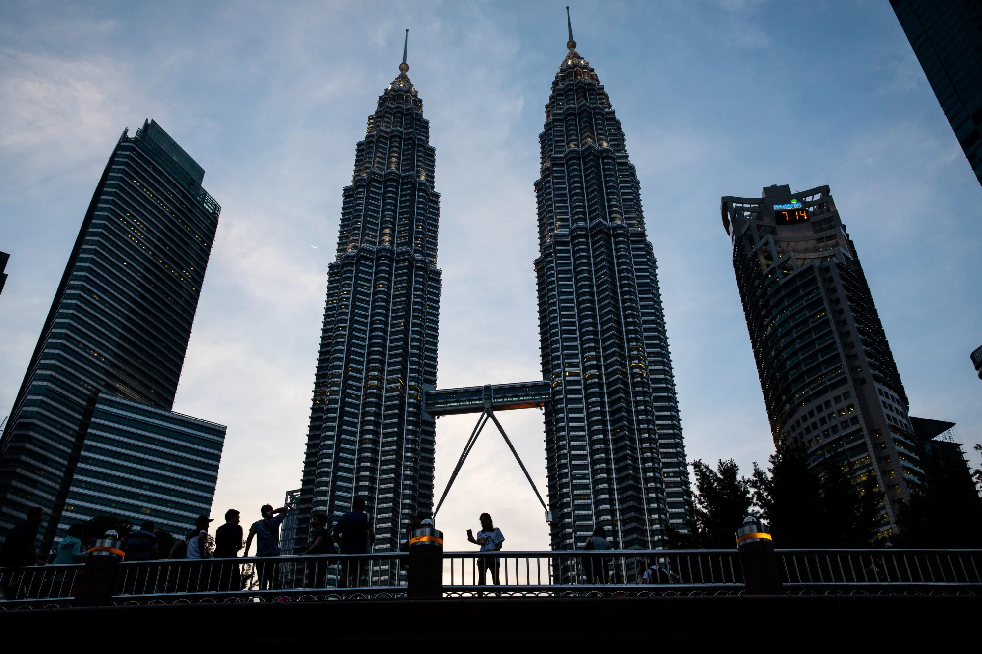 A woman, center, takes a selfie photograph on a bridge in front of the Petronas Twin Towers in Kuala Lumpur.