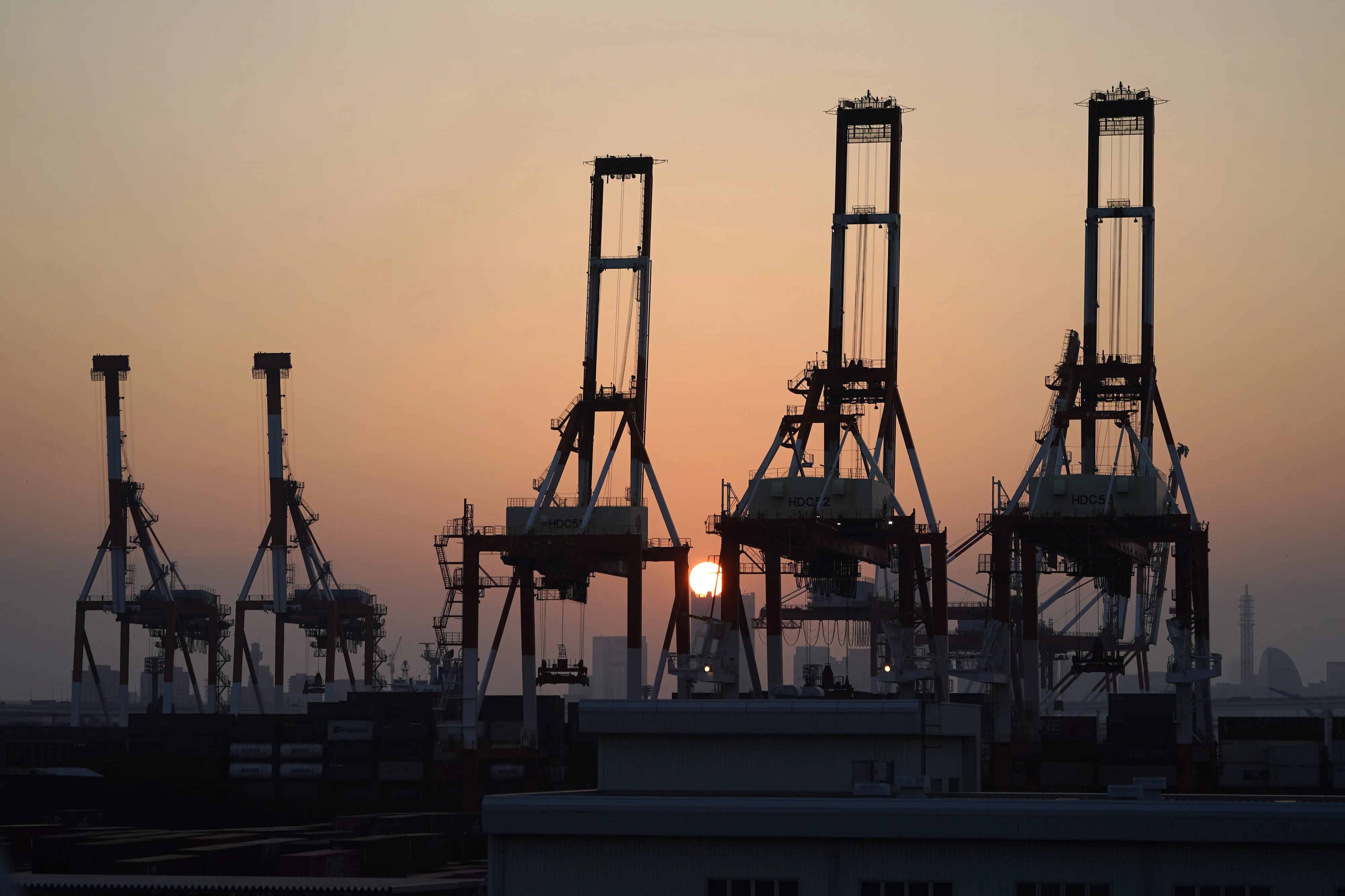 The sun sets behind gantry cranes at a shipping terminal in Yokohama.