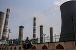 A motorcyclist drives past chimneys and a cooling tower at a coal-fired power plant in the outskirts of Visakhapatnam, Andhra Pradesh, India.