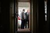 Photo taken from a dark interior of a house looking toward a sunlit front doorway where Keir Starmer talks to an elderly man outside the house