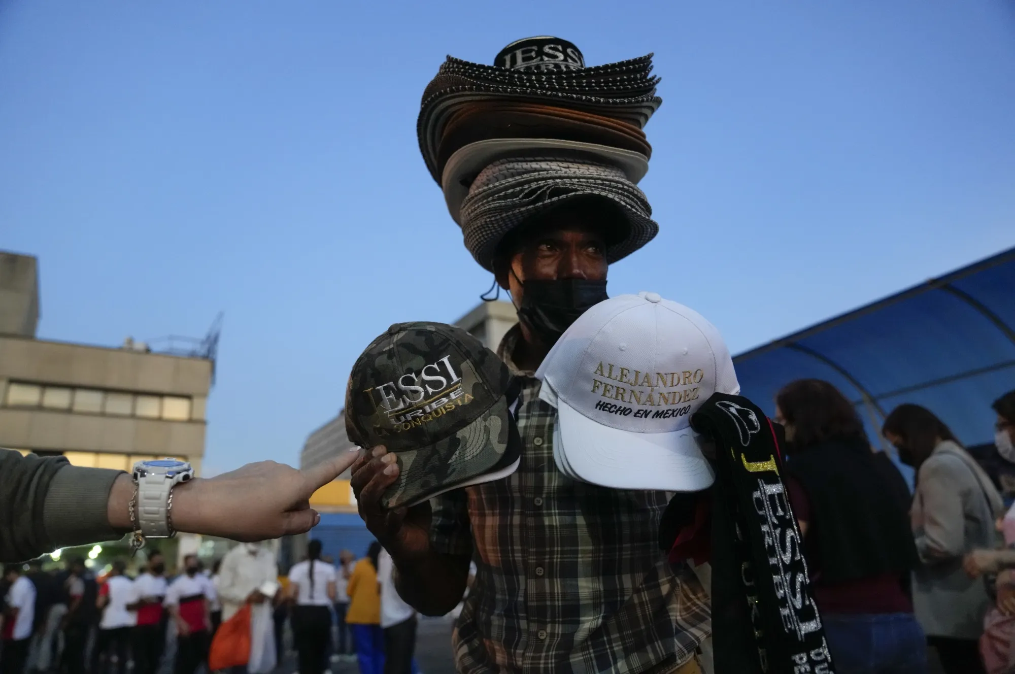  A man sells hats with the name of Mexican singer Alejandro Fernandez and Colombian singer Jessi Uribe as people line up to get into the concert in Caracas, Venezuela, March 3, 2022. Major artists are returning to Venezuelan stages after leaving it out of tours for years and ticket prices are ranging from $55 to $600 dollars. (AP Photo/Ariana Cubillos, File)