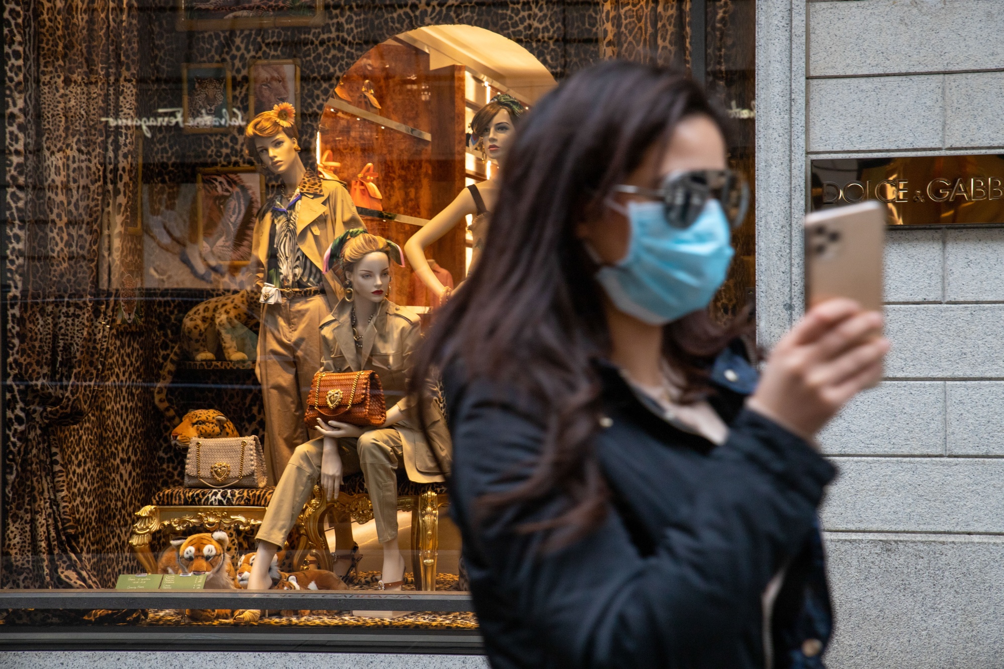 A pedestrian wearing a protective face mask takes a selfie outside a store in Milan on Feb. 25.
