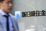 A pedestrian walks past signage for Nippon Steel & Sumitomo Metal Corp.
