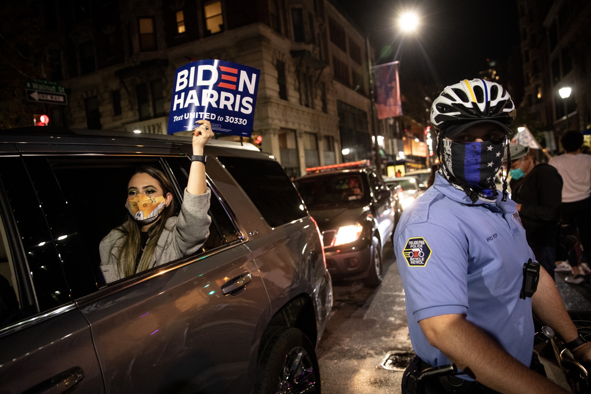 A woman holds a Biden-Harris campaign sign as she passes a police officer during celebrations&nbsp;for President-elect Joe Biden in Philadelphia.