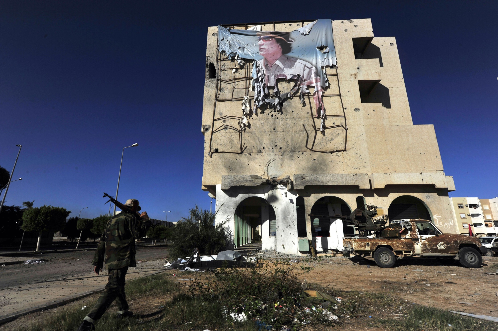 A Libyan National Transitional Council fighter walks under a torn picture of Muammar Qaddafi in Sirte, in 2011.