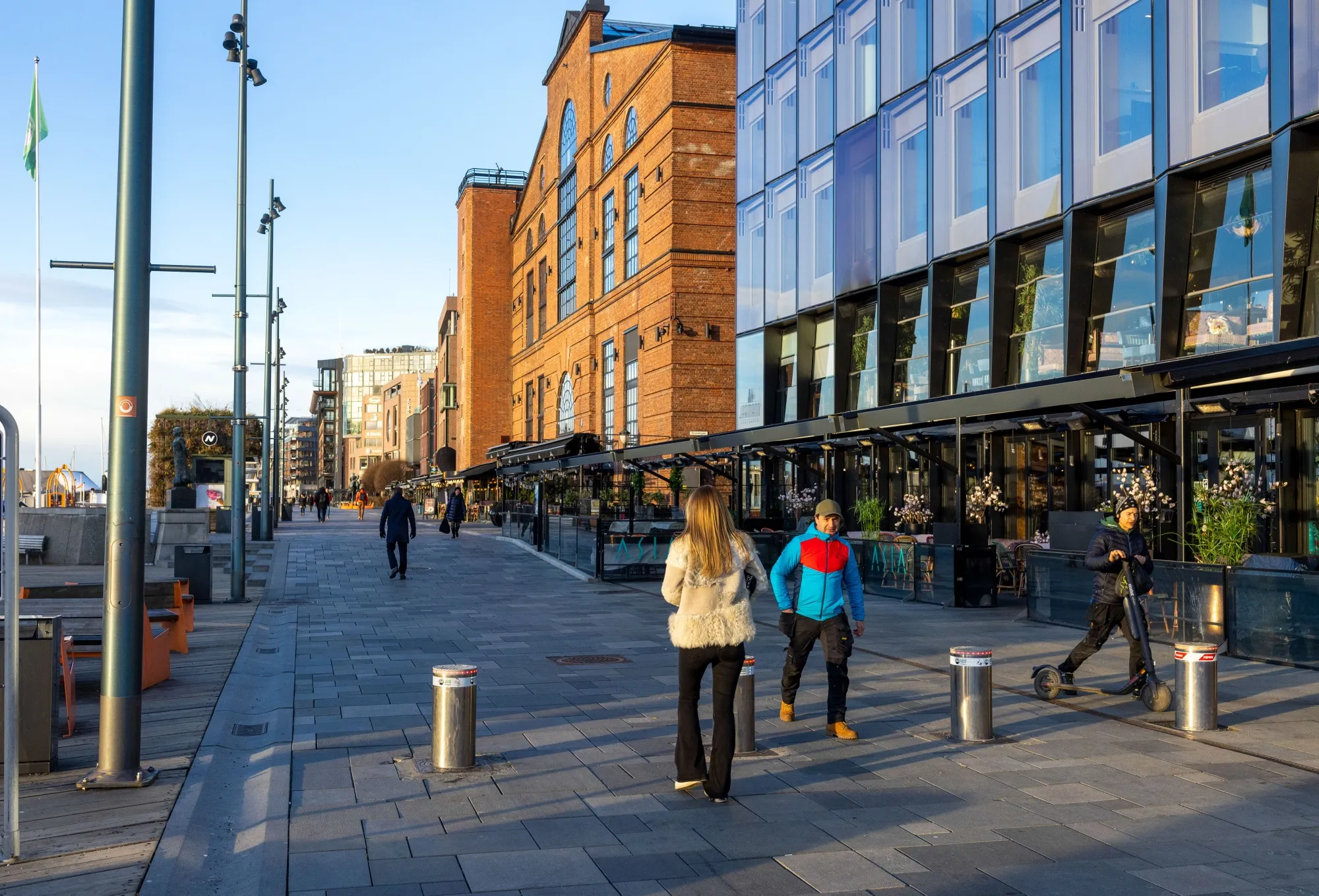 Pedestrians pass restaurants and retail stores in the Aker Brygge district of Oslo, Norway.