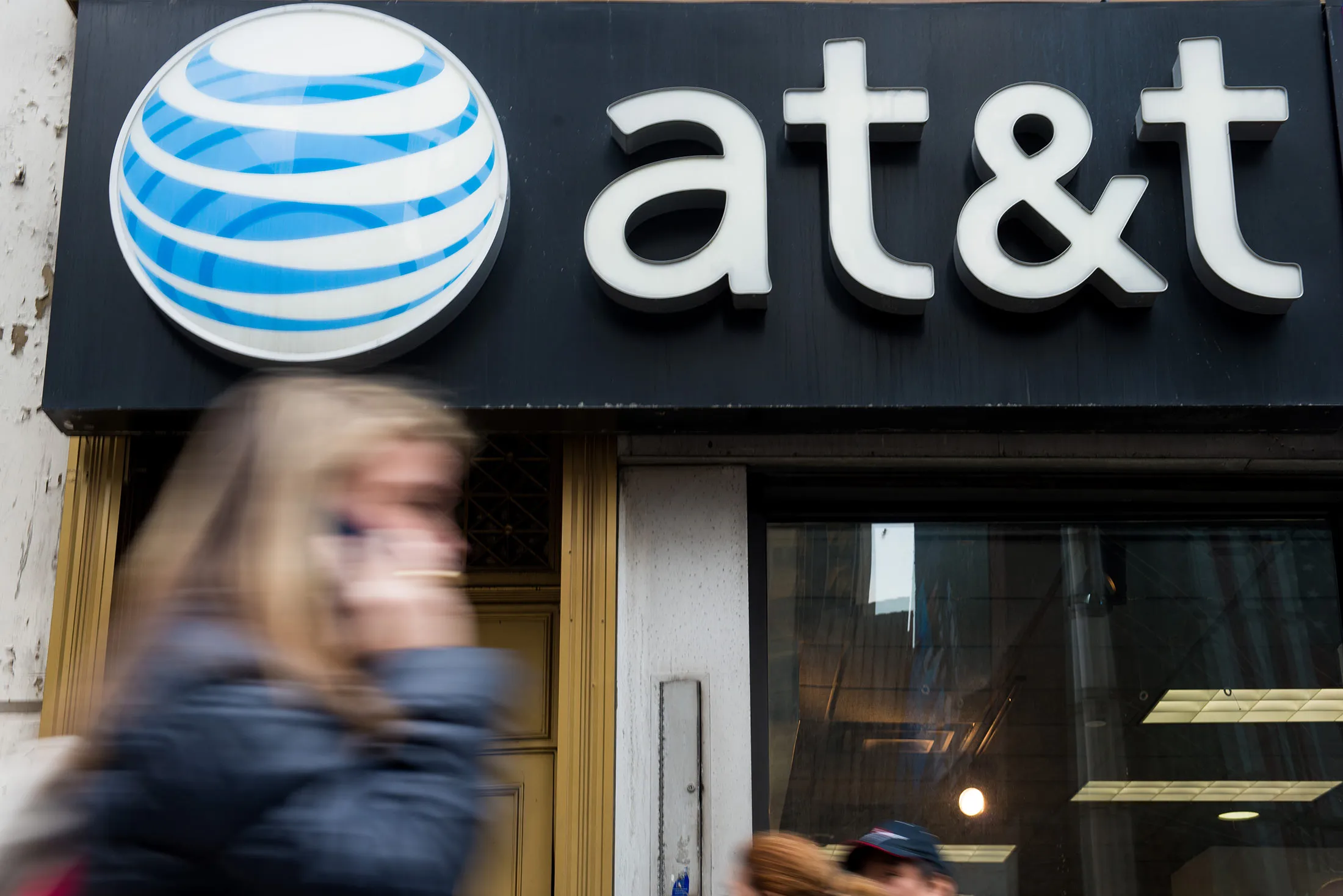 A pedestrian talks on a cell phone while walking past an AT&amp;T Inc. store in New York, on Jan. 27, 2014.
