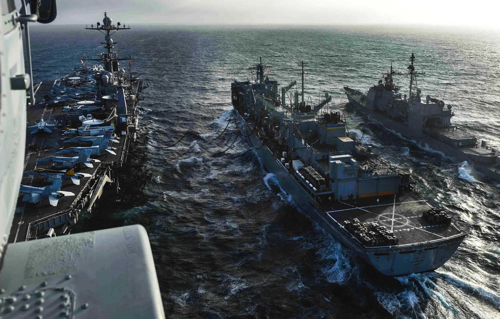 An MH-60S Sea Hawk helicopter flies over an ongoing replenishment at sea between the aircraft carrier USS John C. Stennis, left, the fast combat support ship USNS Rainier, center, and the guided-missile cruiser USS Mobile Bay in the South China Sea, on March 4, 2016.
