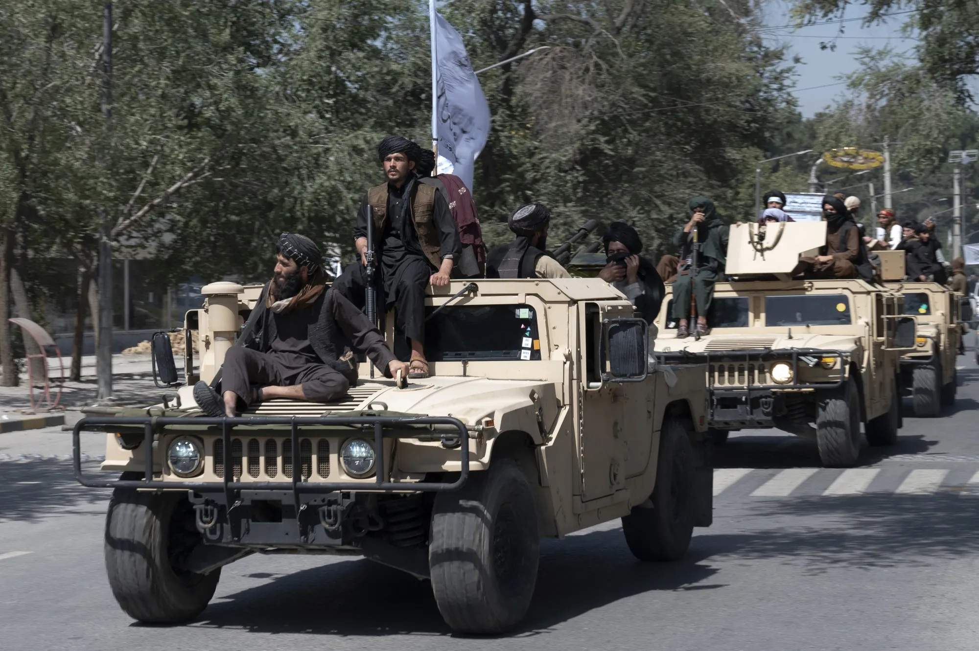 Taliban fighters ride atop armored military vehicles in Kabul.