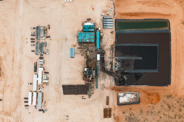 An aerial view of a drilling rig and waste water pit in a dusty dirt landscape